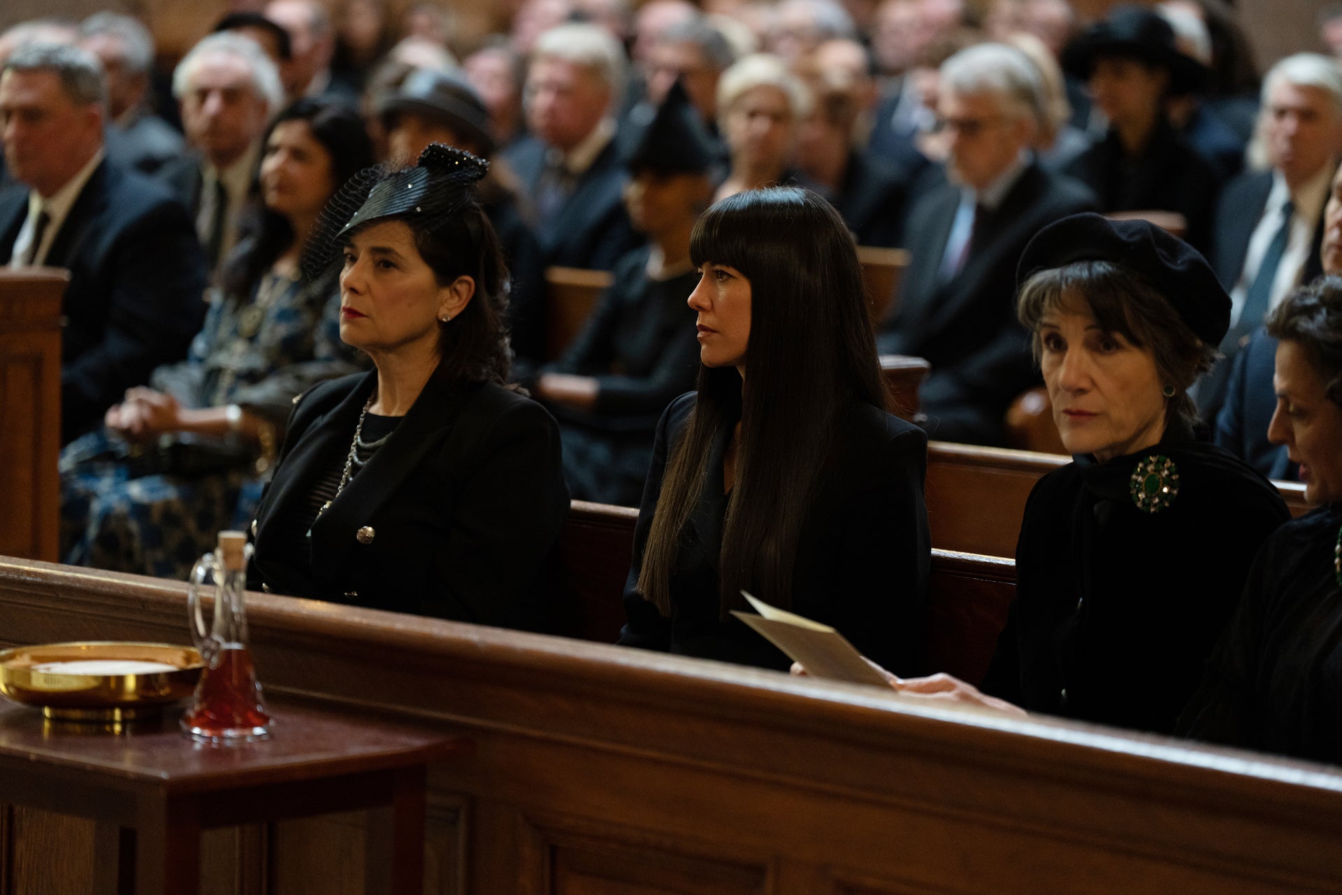 Marcia, Kerry, and Caroline sitting in a pew at Logan's funeral.