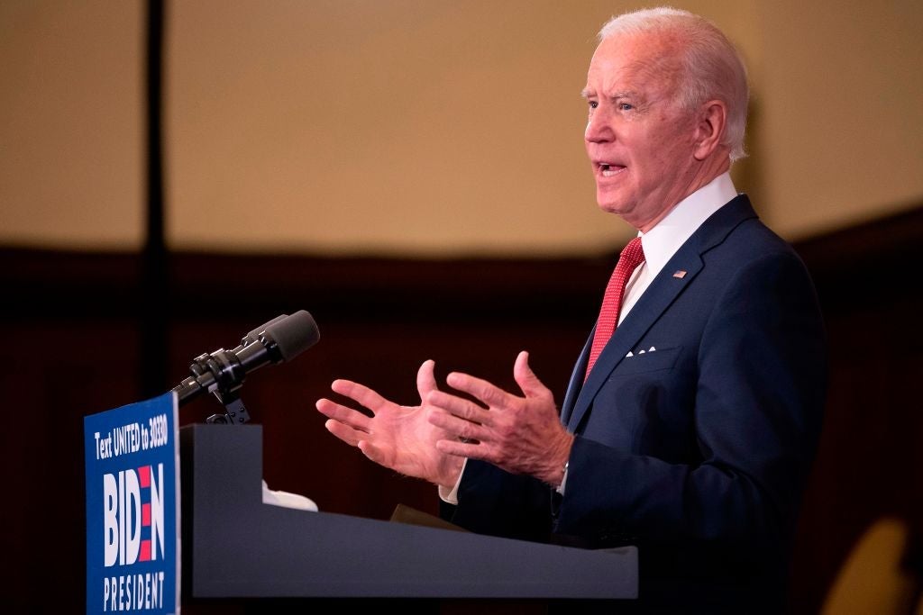 Biden, seen from the side, gestures with both hands while speaking from a lectern decorated with a red, white, and blue Biden for President sign.