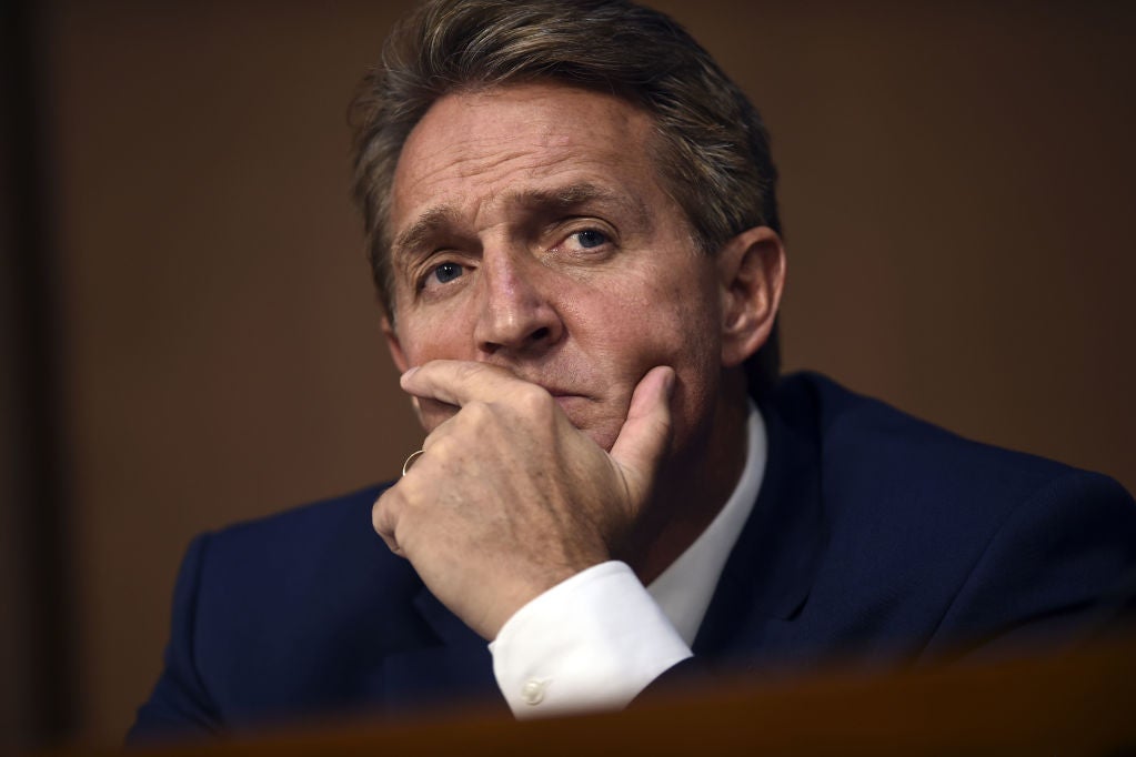 Flake, shot from the chest up while seated, frowns and holds his chin in his left hand.