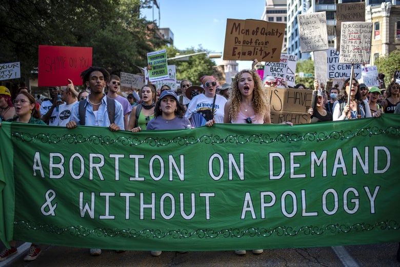 Protesters march while holding up a green banner that says, "Abortion on demand & without apology."
