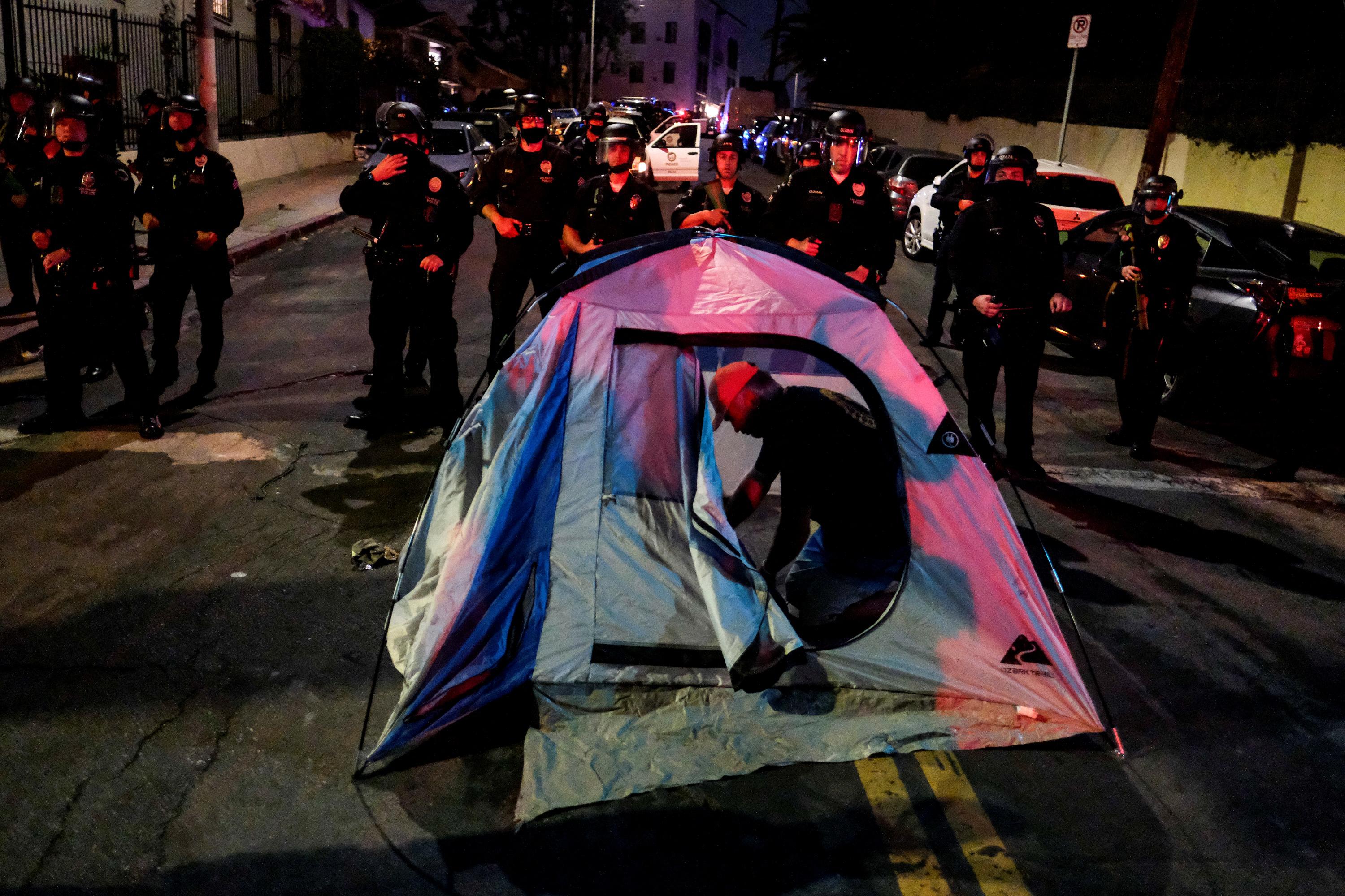 A man sets up a tent in the road in front of a line of police at night.