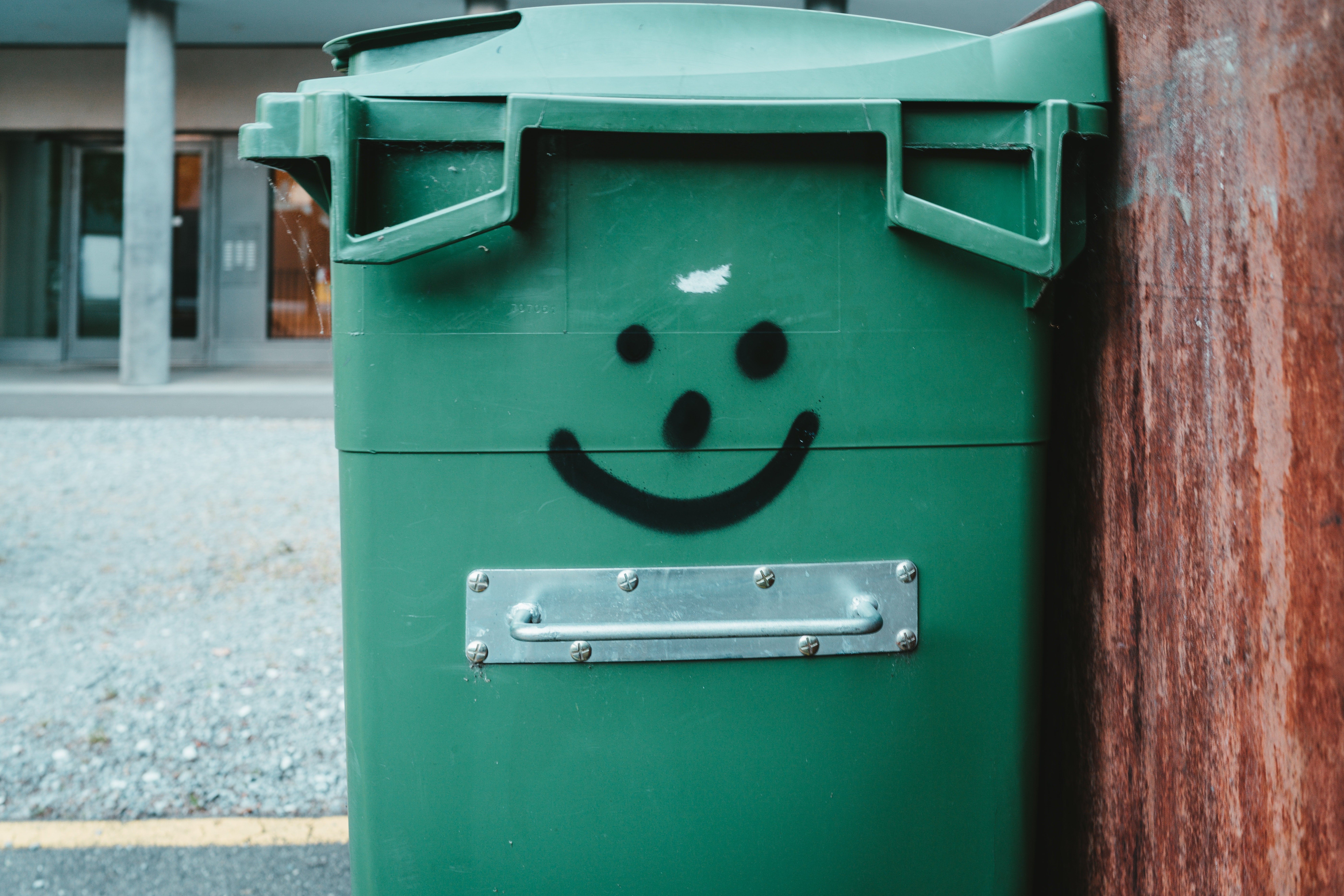 A green trash bin with a smiley face on it.