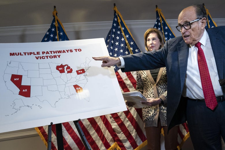 Rudy Giuliani points to an electoral map as he speaks to the press about various lawsuits related to the 2020 election, inside the Republican National Committee headquarters in DC on November 19, 2020. Sidney Powell stands behind Giuliani.