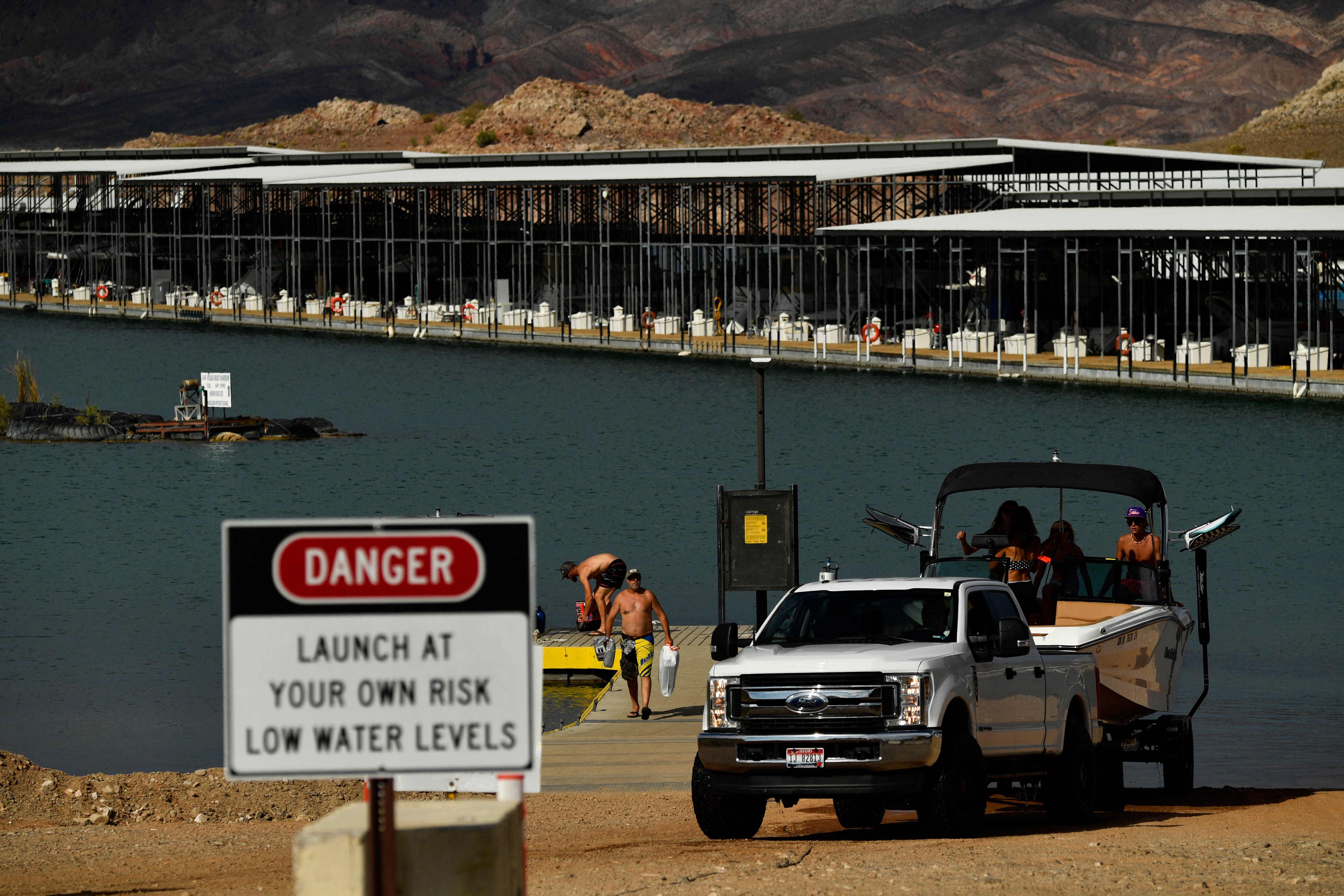 Visitors remove a boat from a boat ramp near a sign that says "DANGER. Launch at Your Own Risk. Low Water Levels."