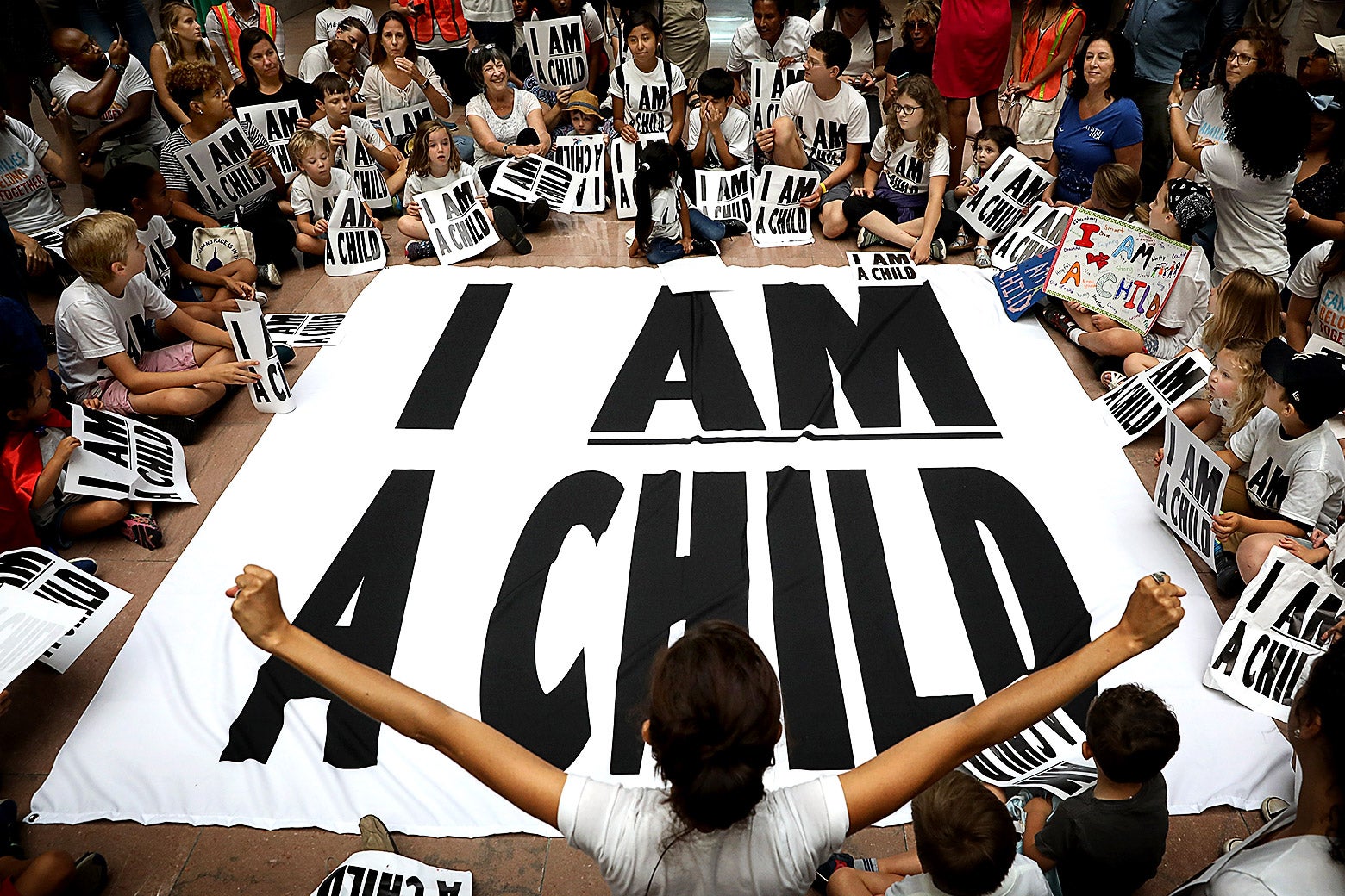People sit around a large sign that says, "I am a child."