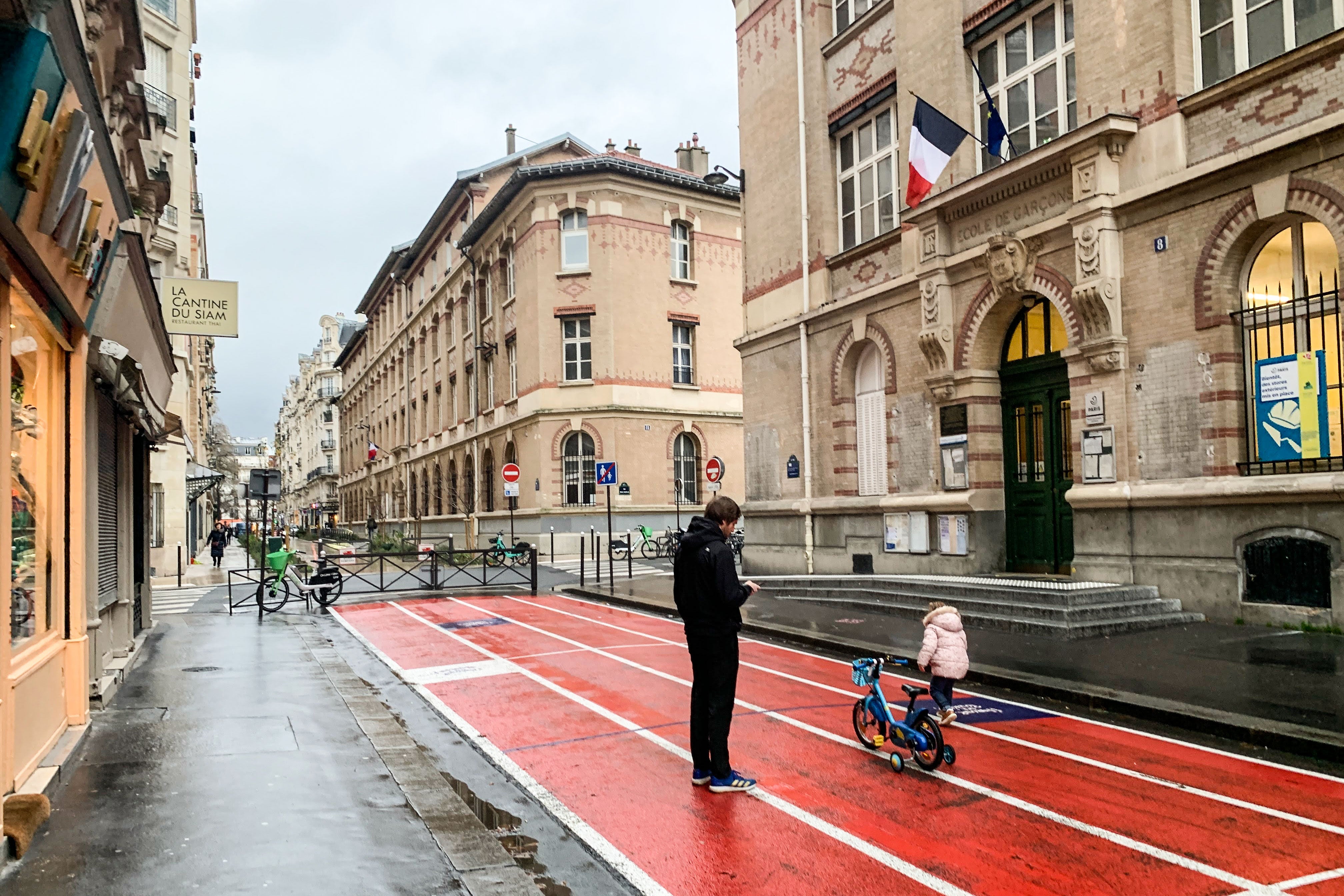 A parent and child, on foot, on an empty, closed-to-traffic street in front of a Paris school.