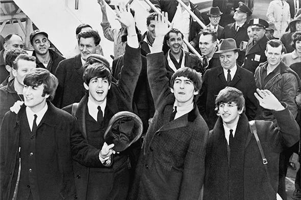 The Beatles standing in a crowd waving to fans.