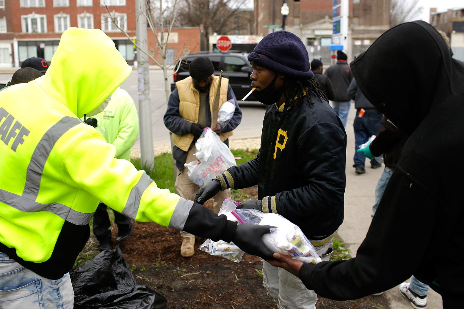 A man in protective gear hands a bag of supplies to a man with a cigarette in his mouth.