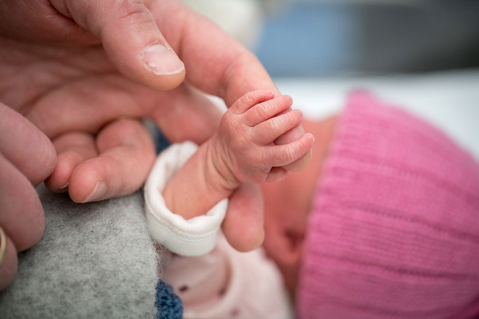 An adult finger lifts up a baby's hand.
