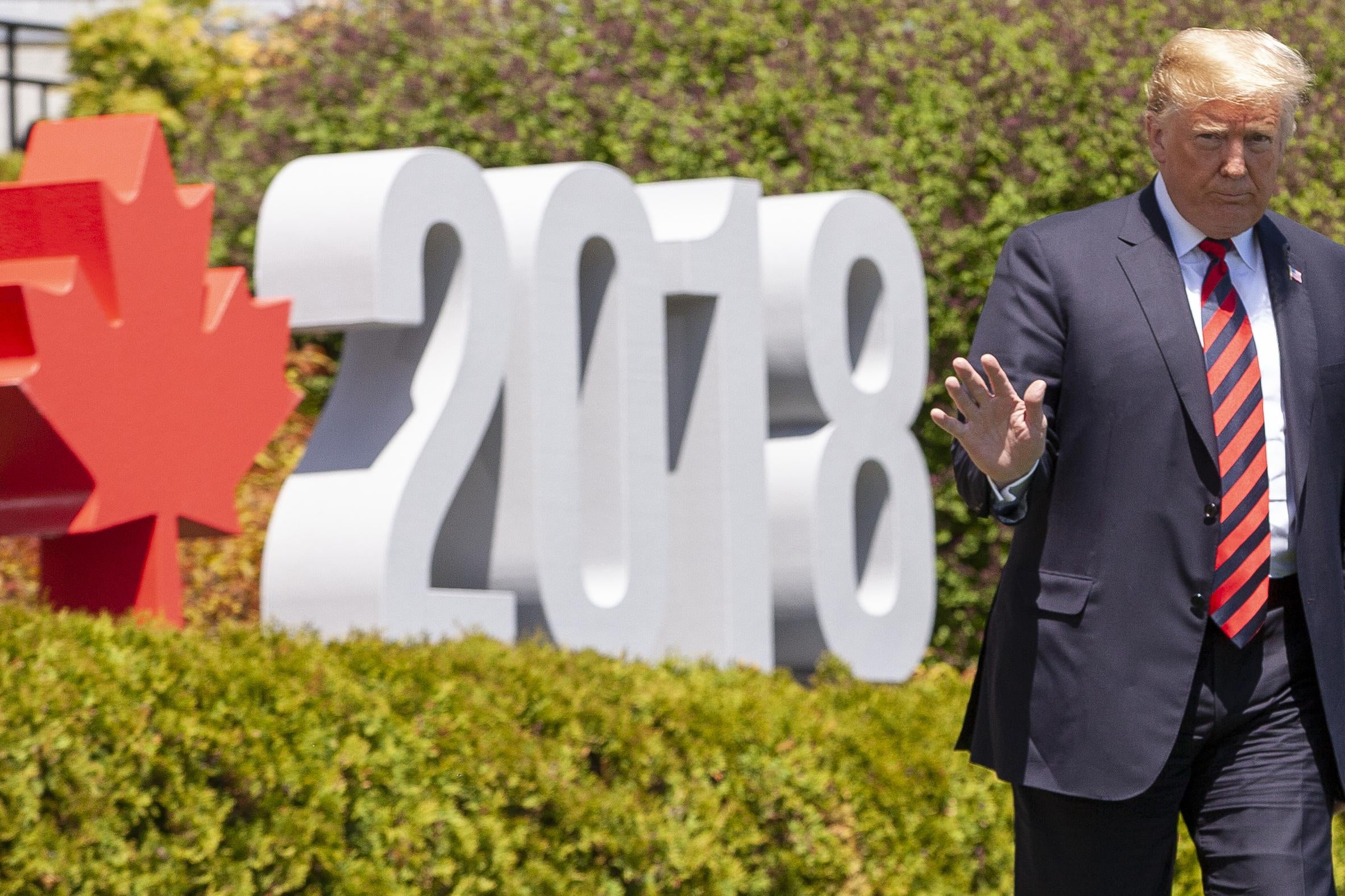 Donald Trump walks by a sign that says 2018 with a red maple leaf.