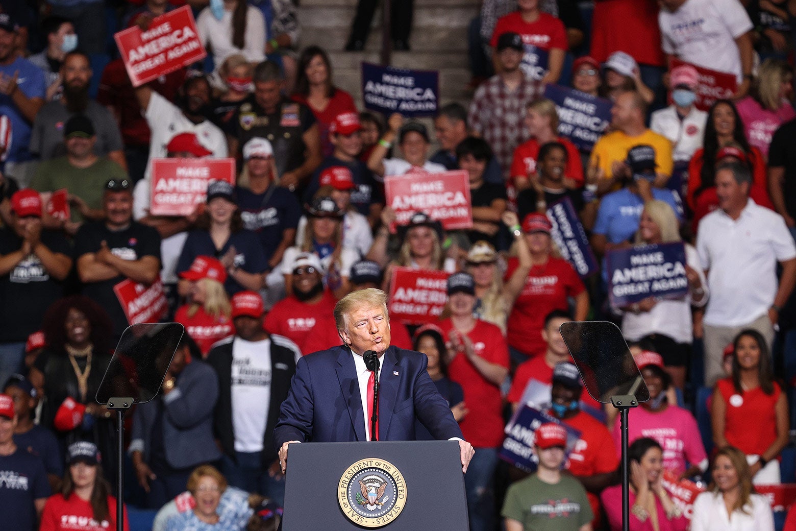 Trump stands behind a podium with a crowd behind him.