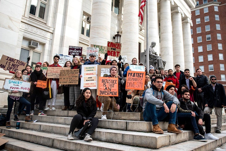 A group of people holding signs sit and stand on the steps of a courthouse. 