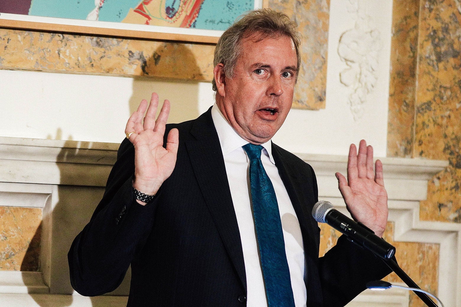 Darroch holds up his hands mid-speech at a podium.