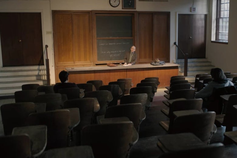 Elliot at the front of a college classroom with old chairs in it.