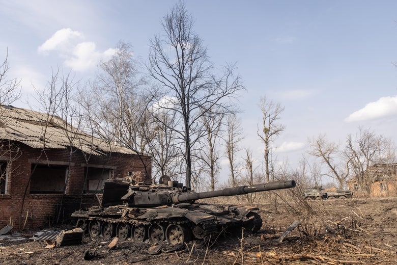 A destroyed tank next to a brick structure and barren trees