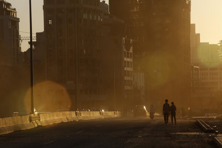People at sunset walk on the highway amid damaged buildings.