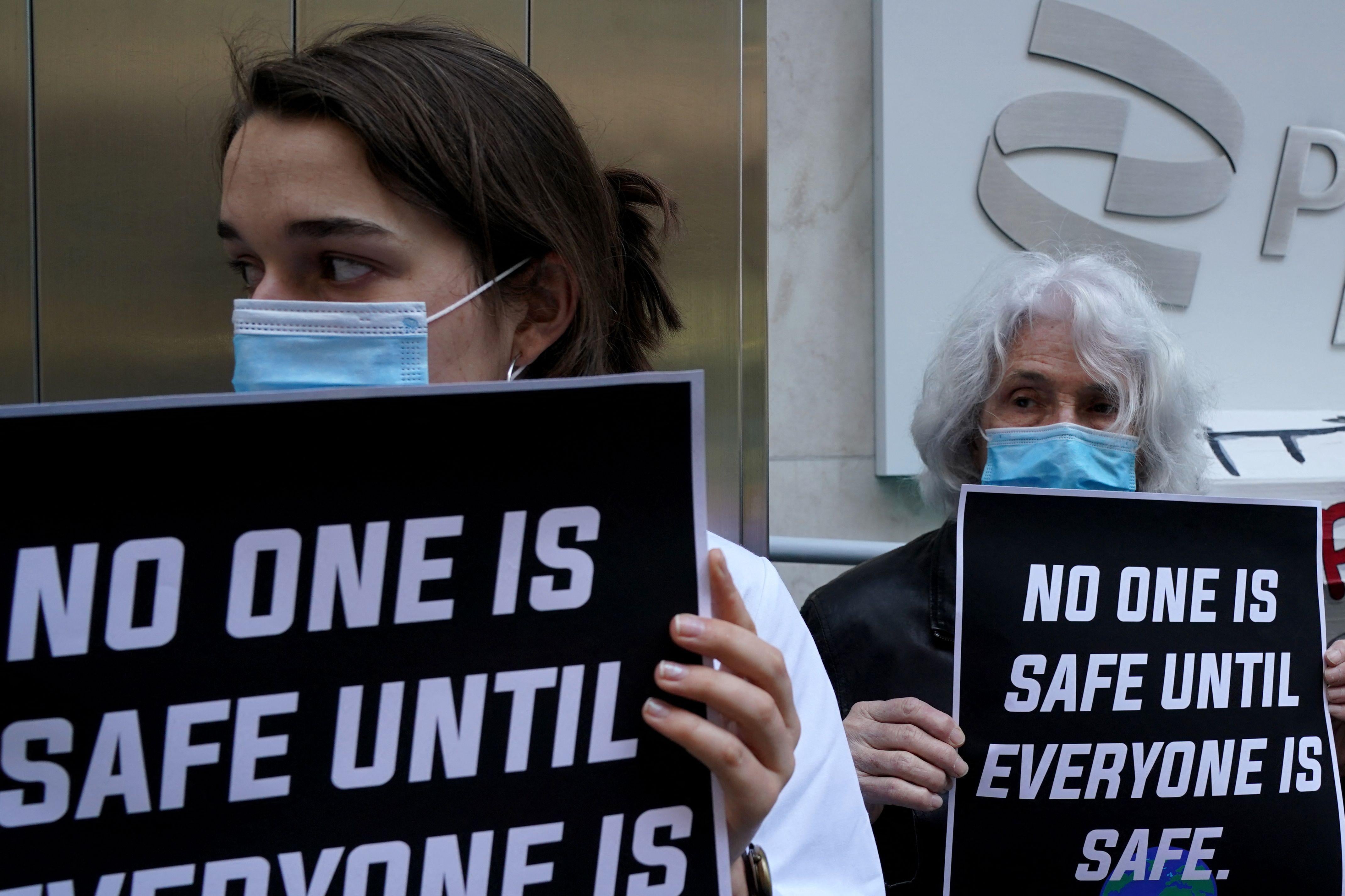 People hold signs that say "No one is safe until everyone is safe" in front of the Pfizer building in New York