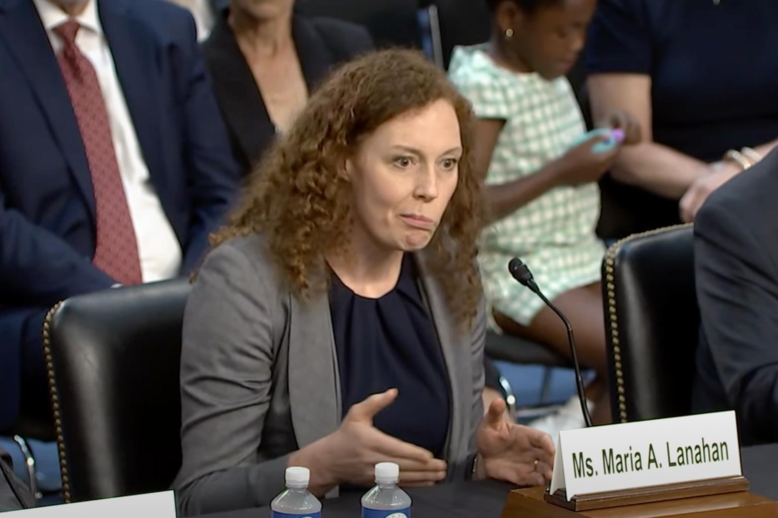 A white woman with dark curly hair at her Senate hearing, with her mouth agape.