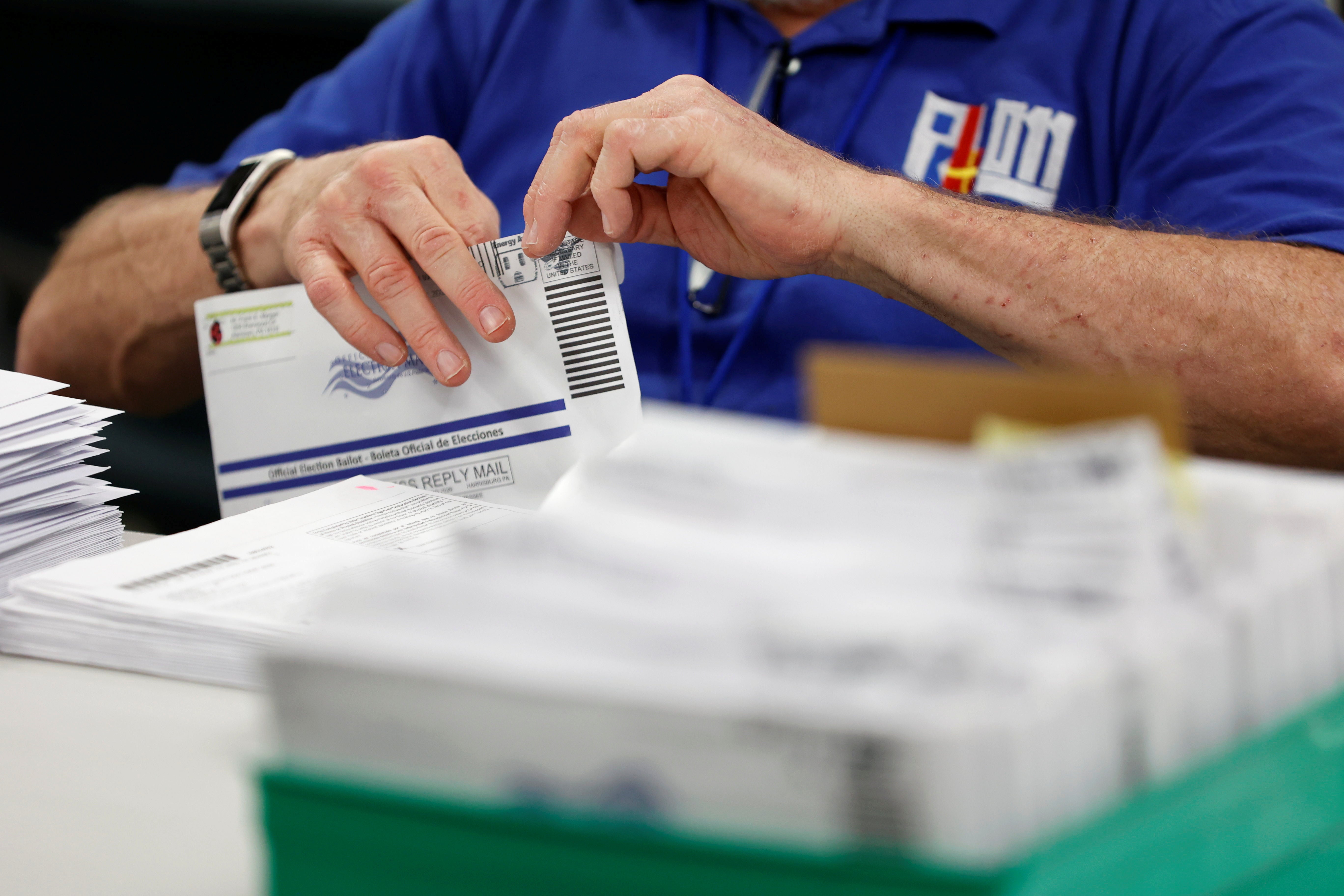 An election worker's hands are seen opening a mail-in ballot taken from a box of ballots.