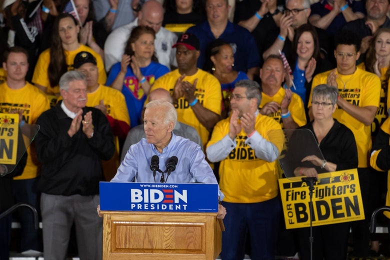 Biden speaks at a podium, with a crowd of Teamsters behind him wearing shirts and holding signs that say Fire Fighters for Biden.