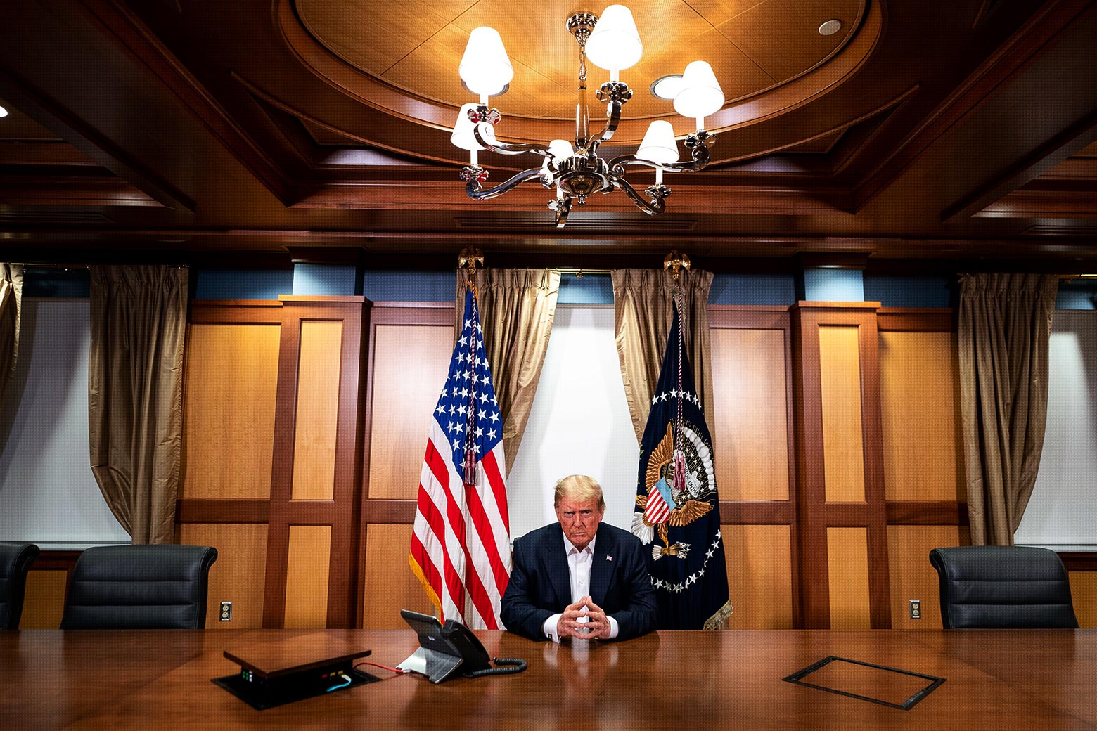 Trump sits hands clasped at a large conference room table with a speaker phone near him.