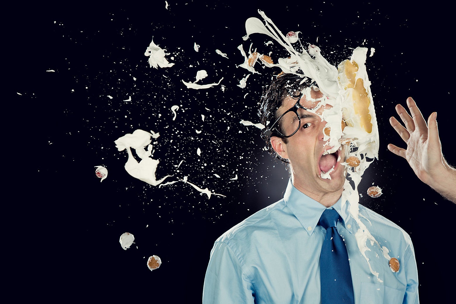 A man with glasses gets pied in the face.