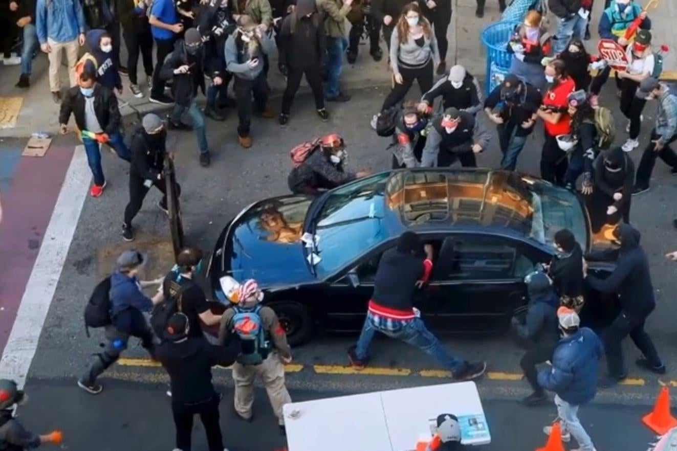 A crowd of protesters surrounds a car.