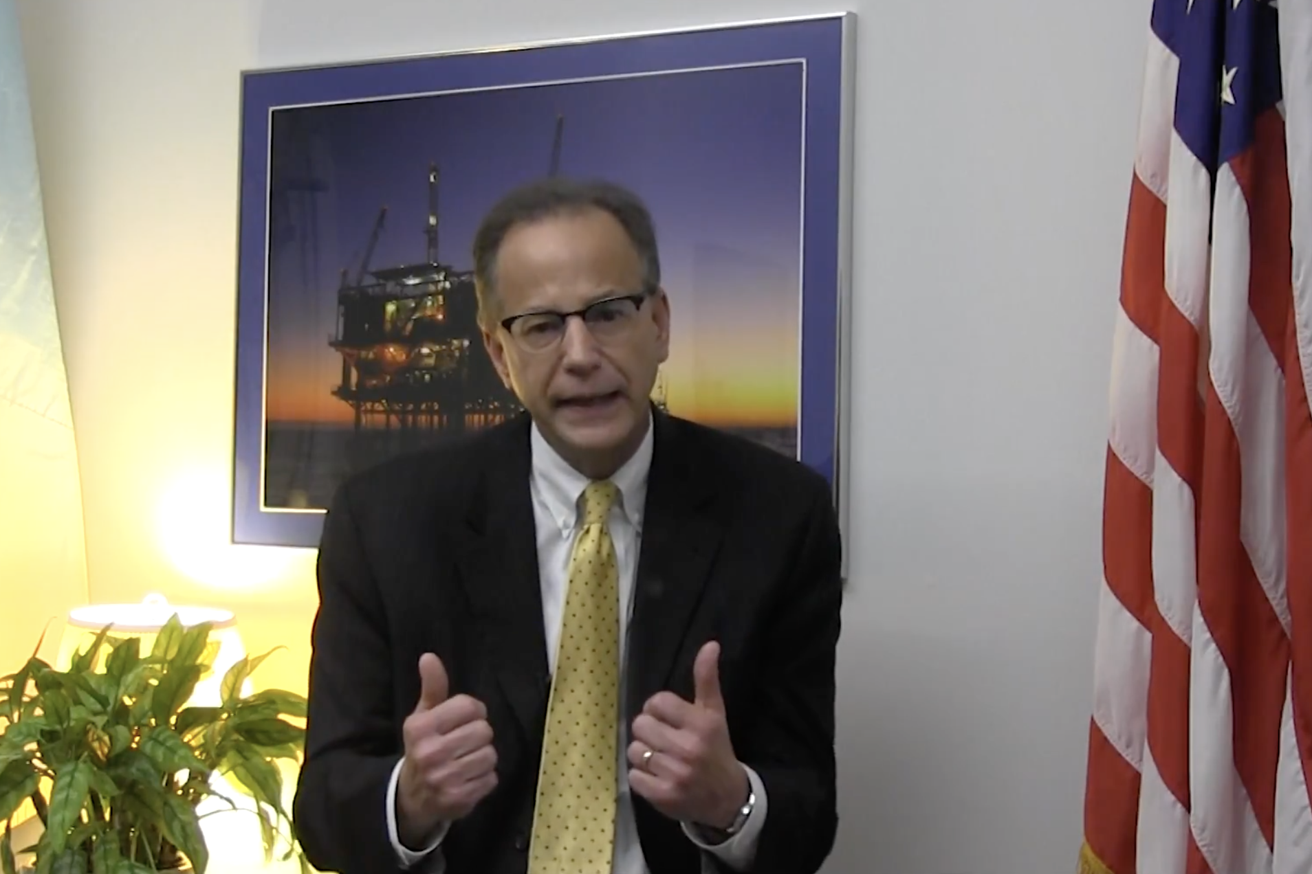 Scott Angelle gives a thumbs=up in front of photo of an oil rig