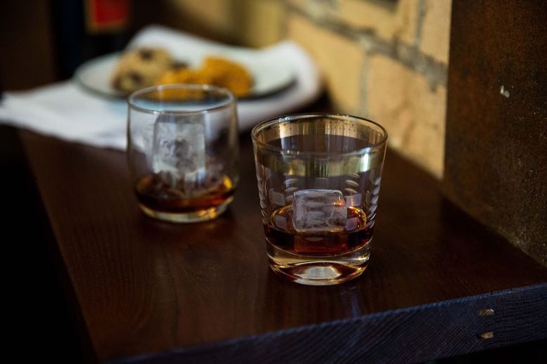Two glasses of brown-colored Cynar on a dark wood panel