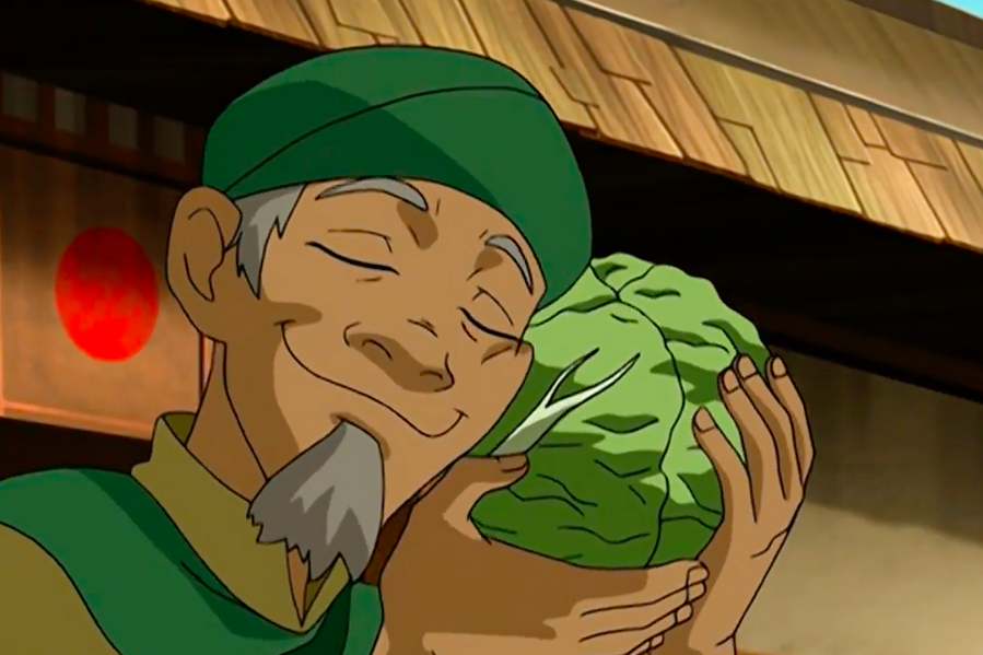 A cartoon man with a green cap and a gray beard lovingly cradles a head of cabbage against his cheek.