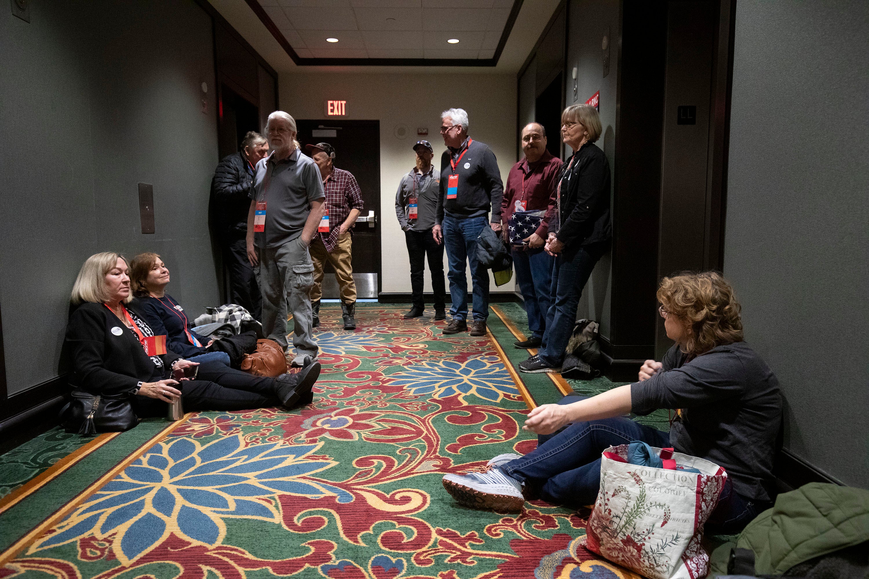 Ten people in a hotel hallway; several are sitting on the floor. 