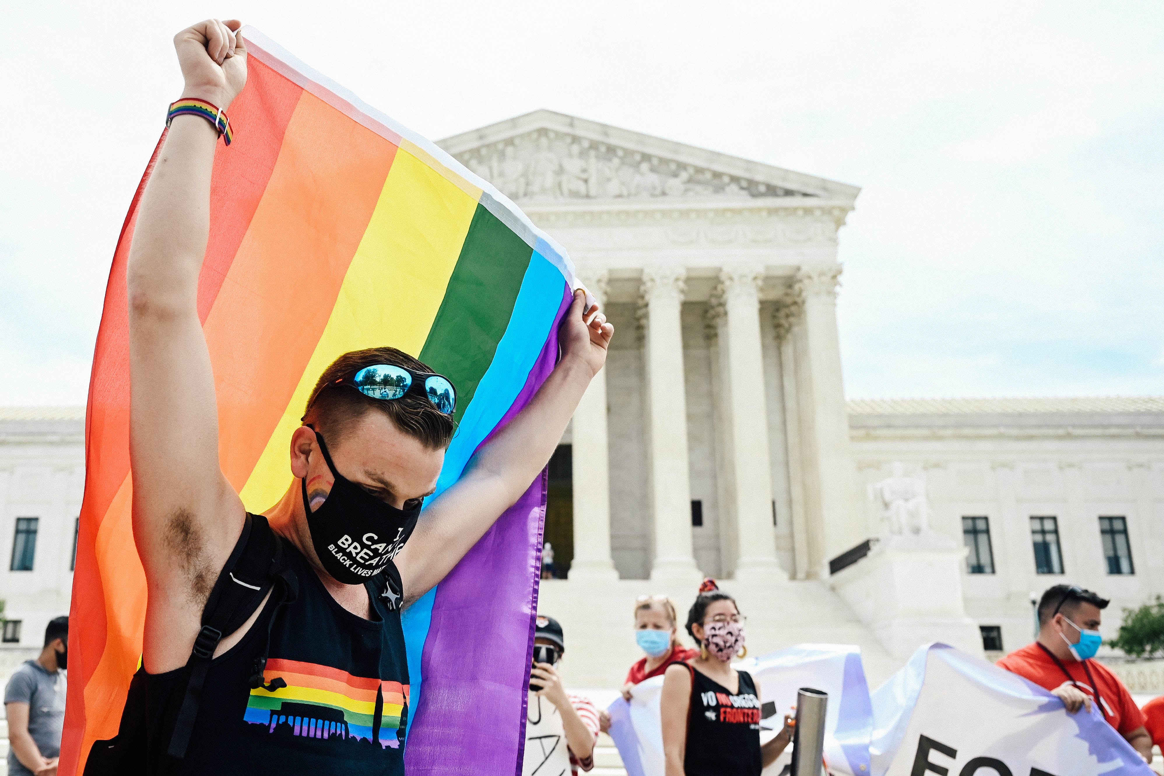 Person holding up a rainbow flag in front of the Supreme Court building