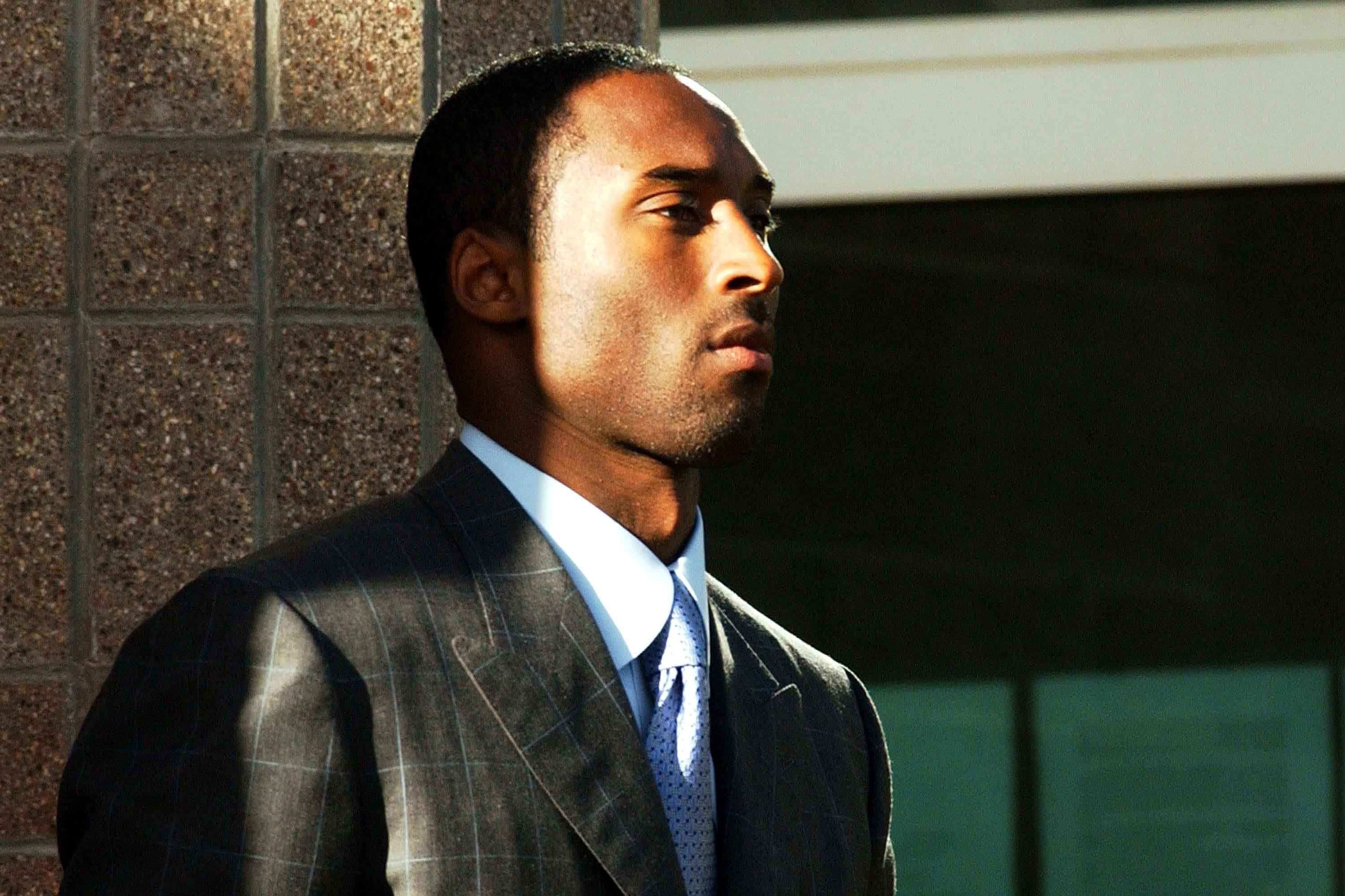 Kobe Bryant standing in a suit in the sun outside the courthouse, with a serious expression on his face.