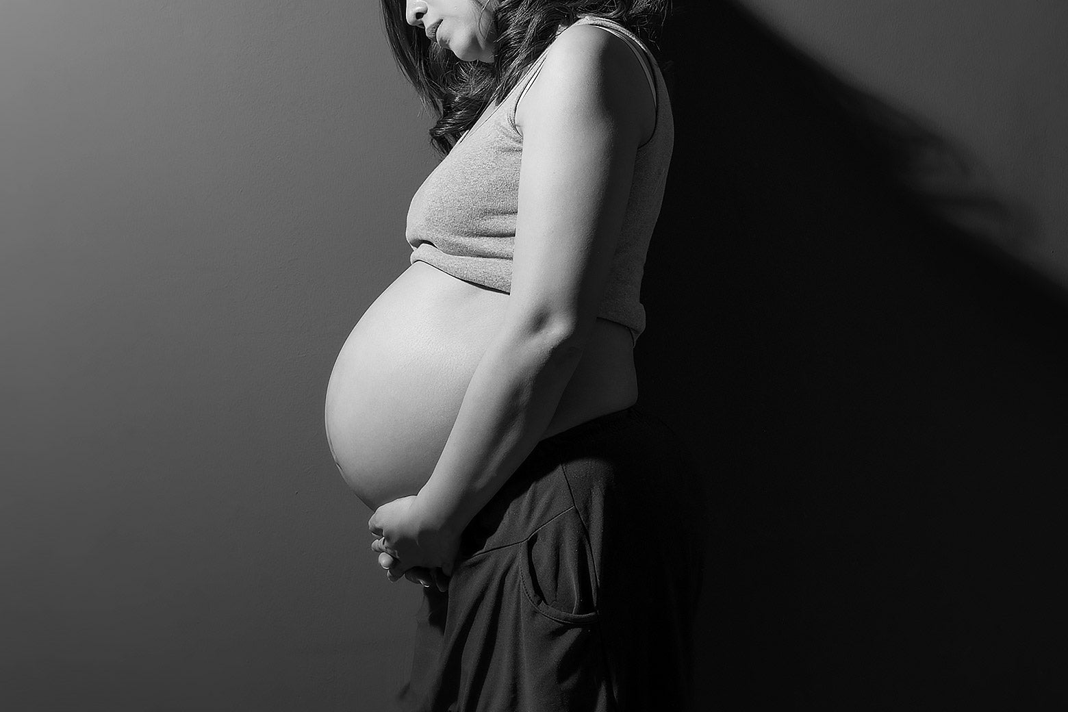 A lonely, pregnant woman leaning against a wall cradling her stomach.