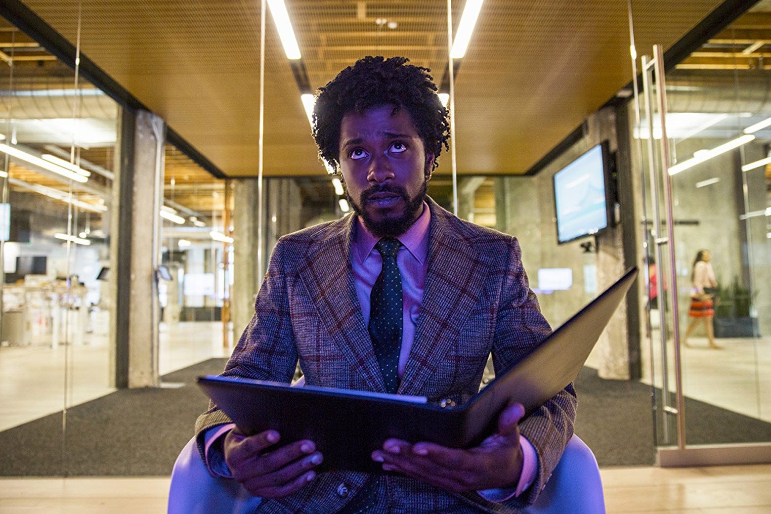 Lakeith Stanfield’s character holds open a binder, while in an office setting.