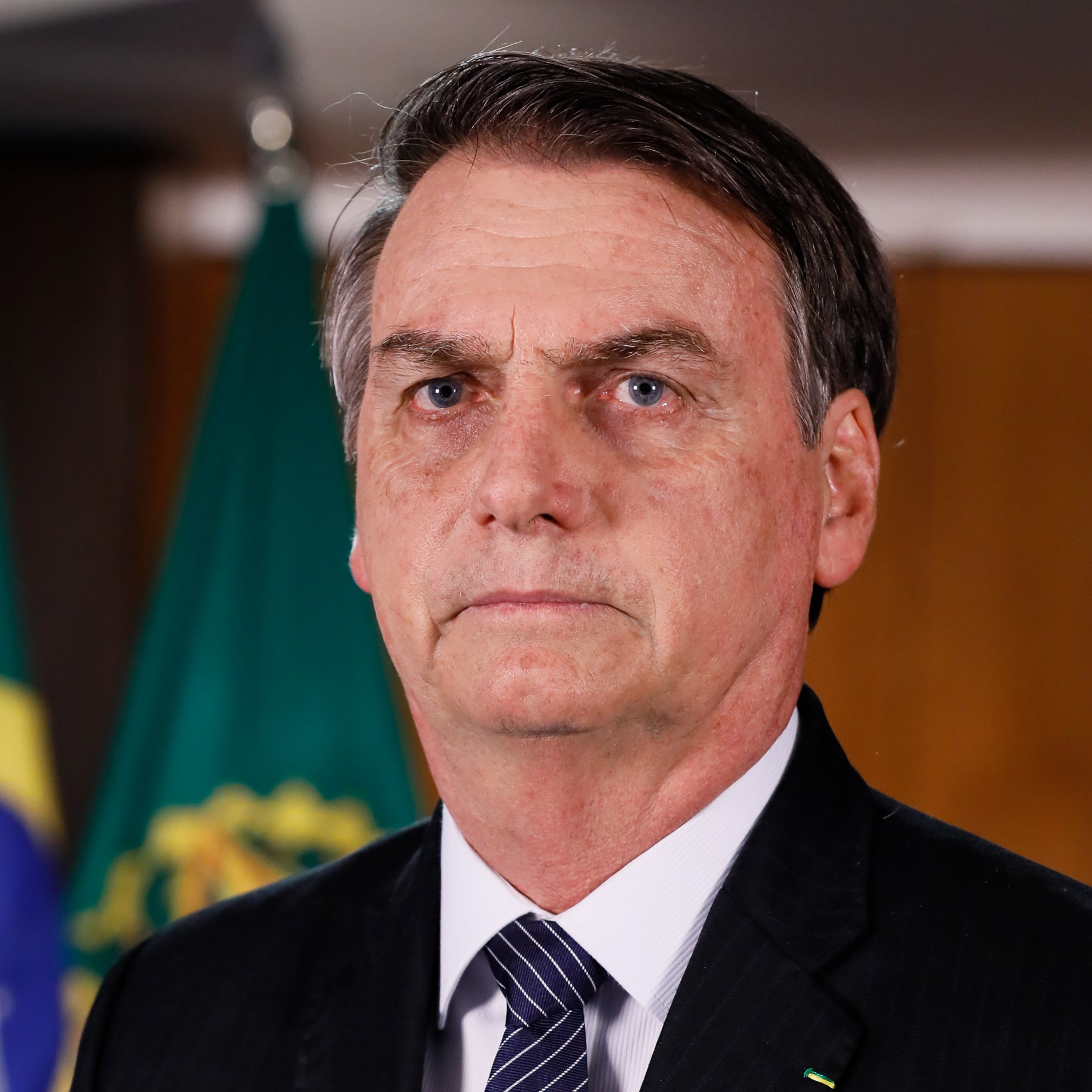 Bolsonaro stares at the camera with a sort of serious but hangdog expression.
