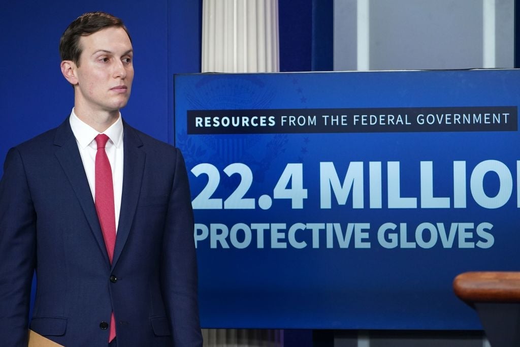 Kushner stands beside a video screen displaying a graphic which claims the federal government has shipped 22.4 million protective gloves.