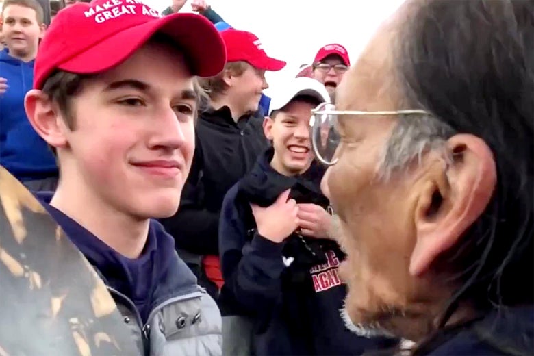 Sandmann, who is wearing a Make America Great Again hat, smiles at Phillips.