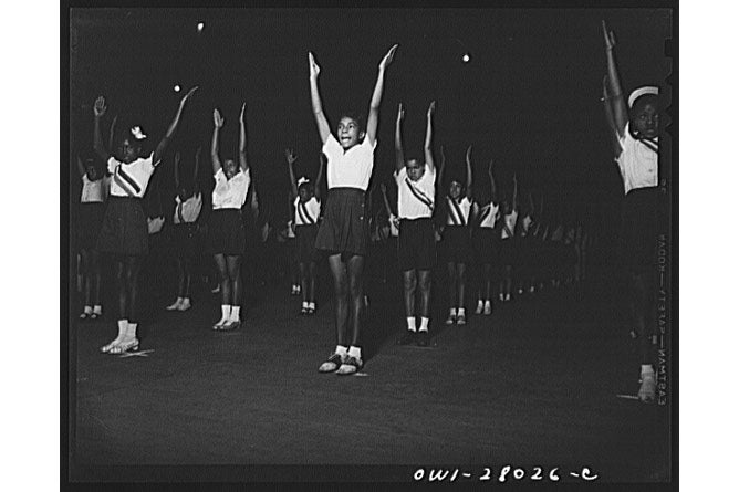 A black-and-white photo showing lines of students doing exercises in a gym