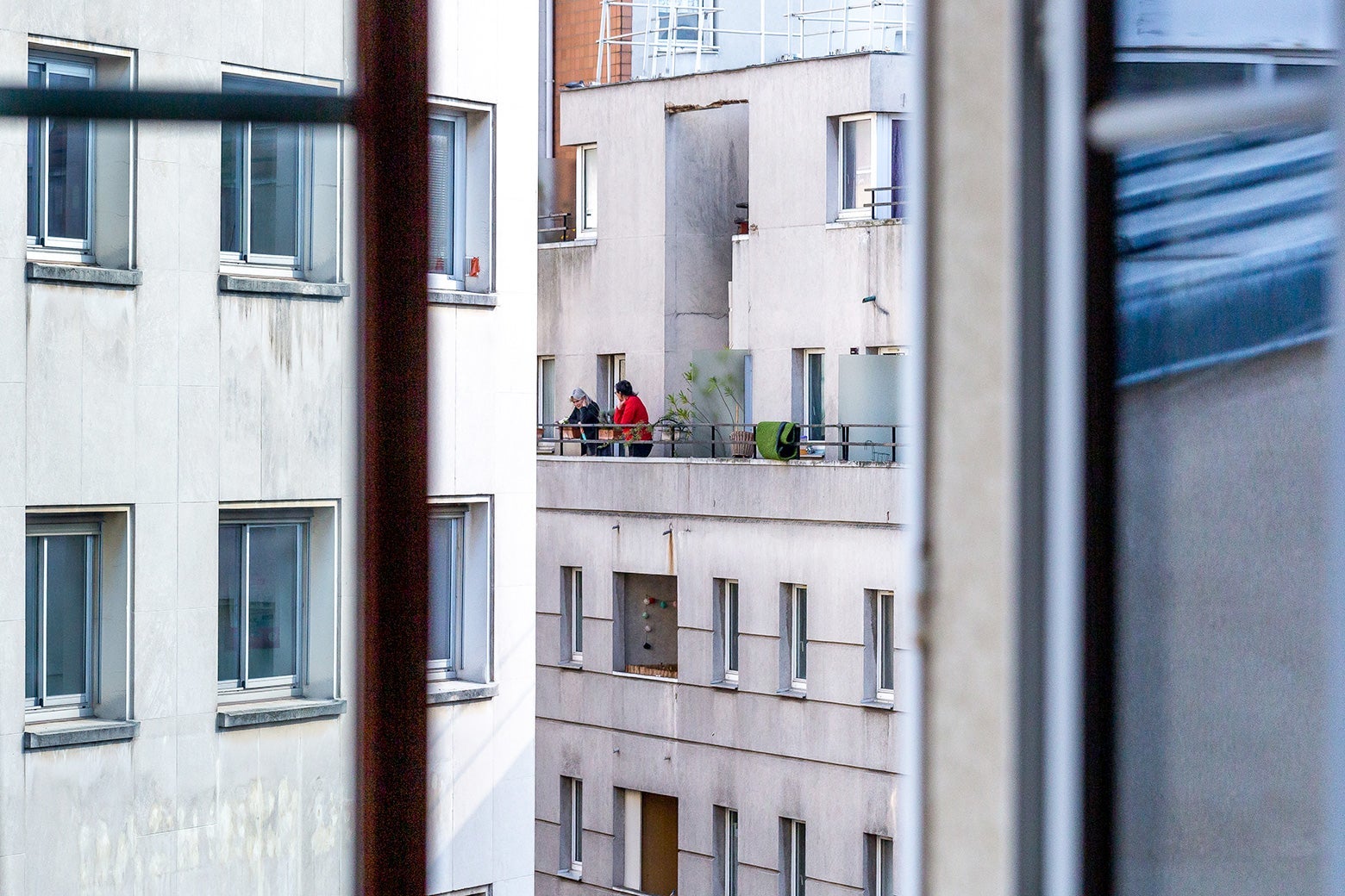 A Paris apartment complex seen out a window, with two people standing on a balcony.