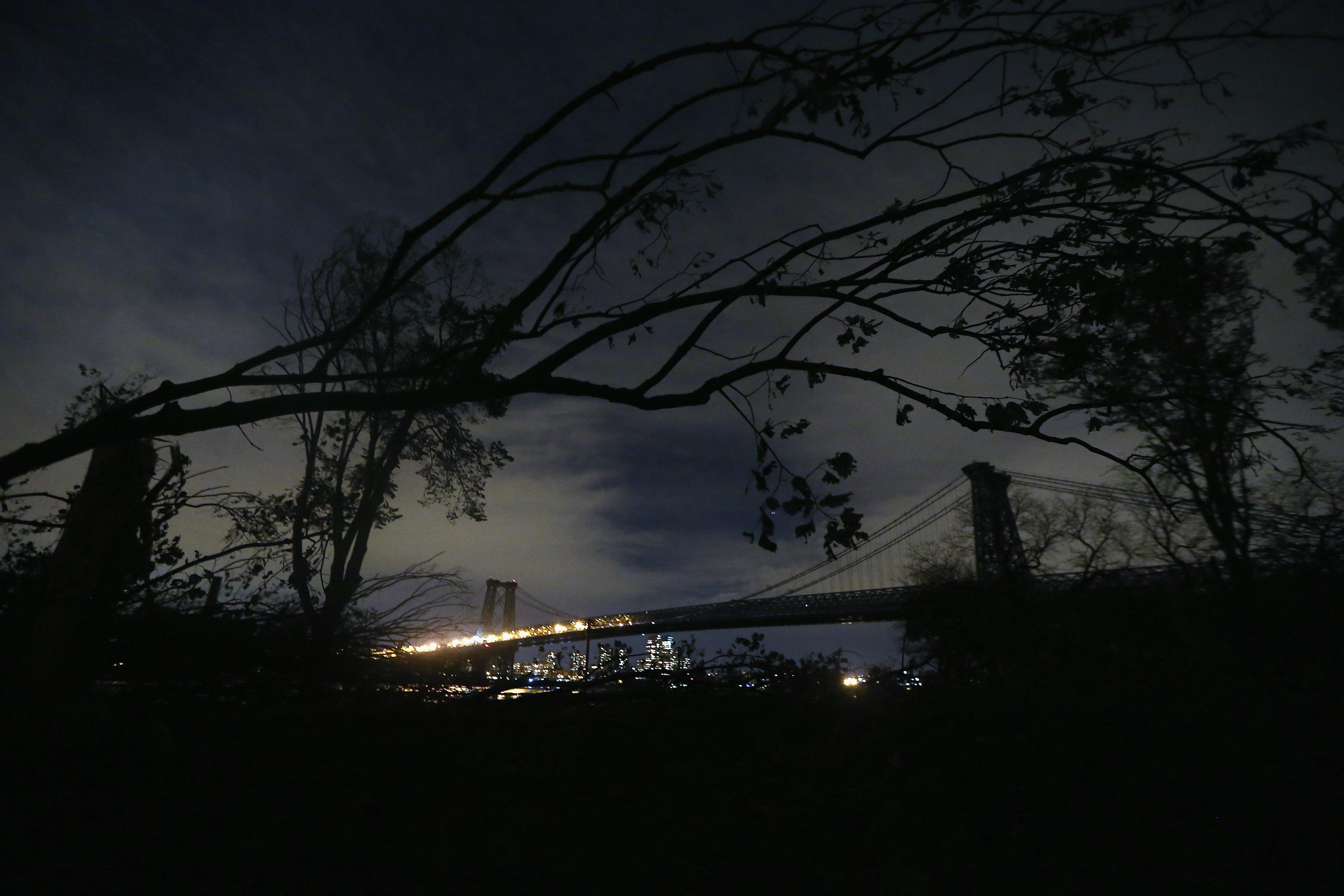 Parts of a fallen tree dangle in front of the Williamsburg Bridge, lit on the Brooklyn side (L) but darkened on the Manhattan side on November 1, 2012 in New York.