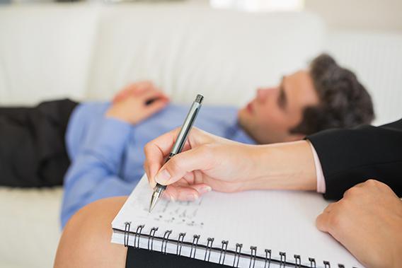 Man lying on a sofa while with therapist making notes