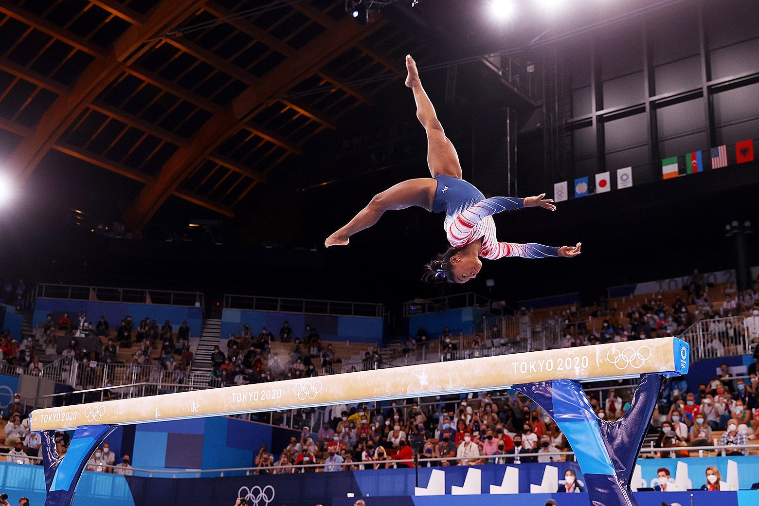 Biles upside down in midair as she does a flip on the balance beam