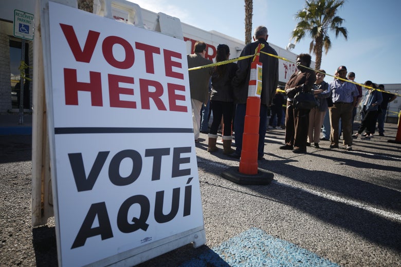 A sign reading "Vote Here" and "Vote Aquí" sits in front of a voting line.
