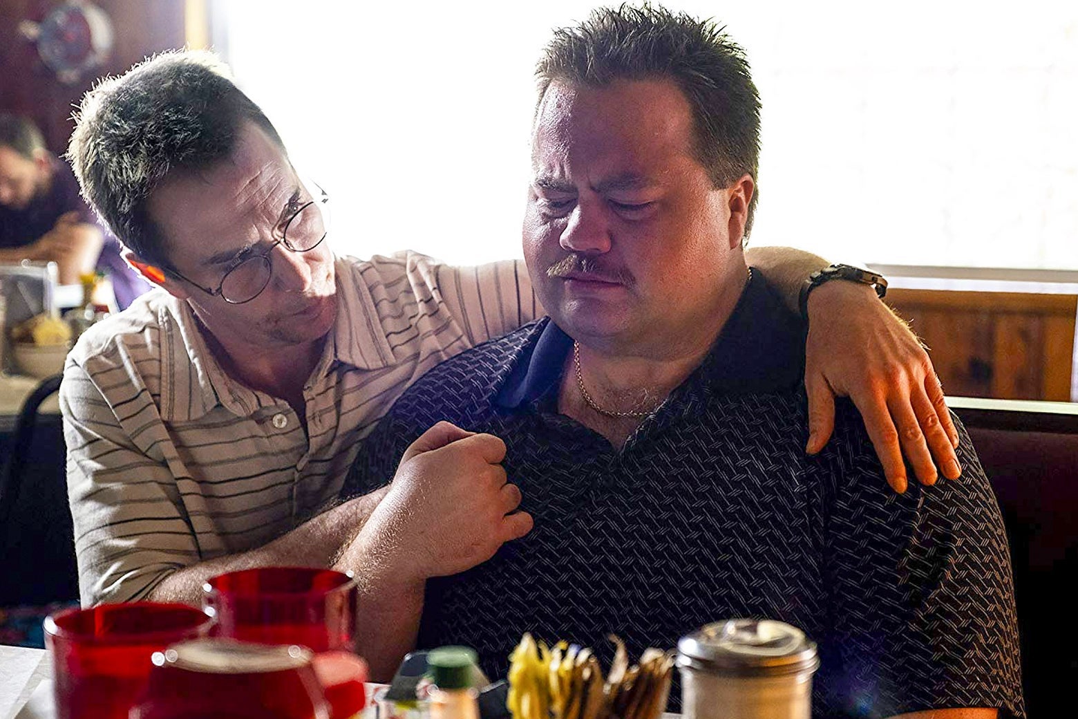 Sam Rockwell puts an arm around a visibly anguished Paul Walter Hauser while they sit in a booth in this still from Richard Jewell.