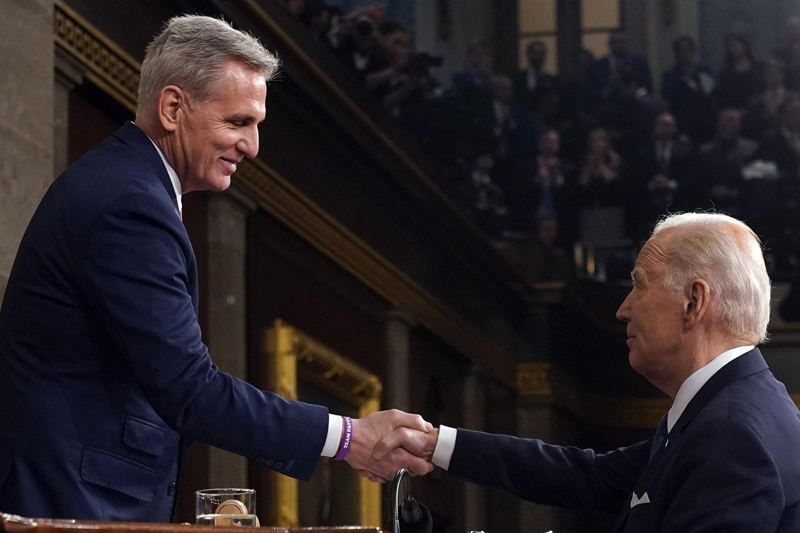 President Joe Biden reaches up to shake hands with House Speaker Kevin McCarthy.