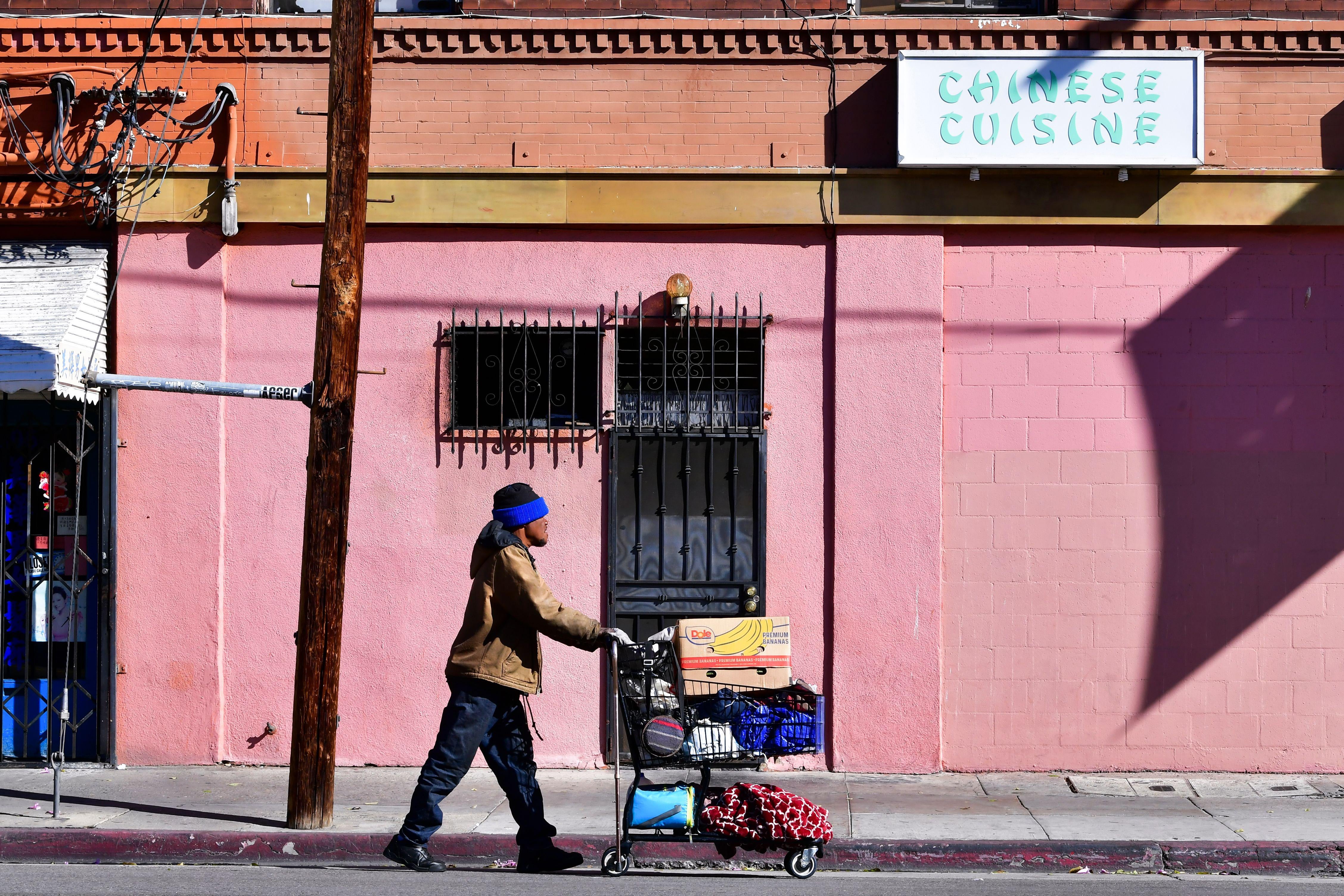A homeless man pushes a cart full of his belongings along an empty sidewalk