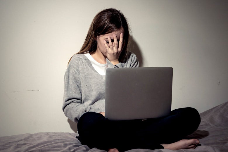 A college student facepalming with a laptop in front of her.