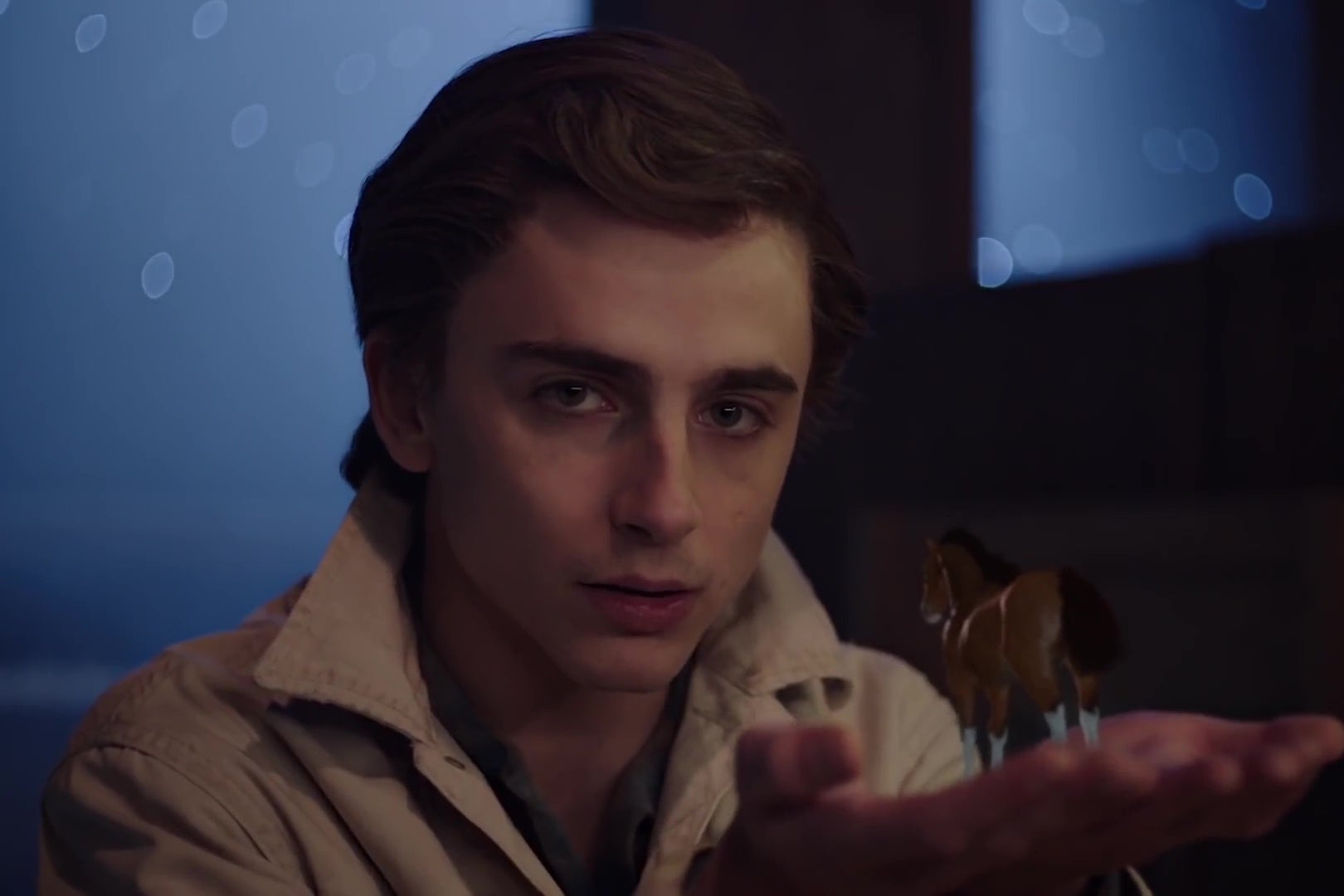 Timothee Chalamet, dressed as a cowboy, holds a tiny claymation horse in the palm of his hand.