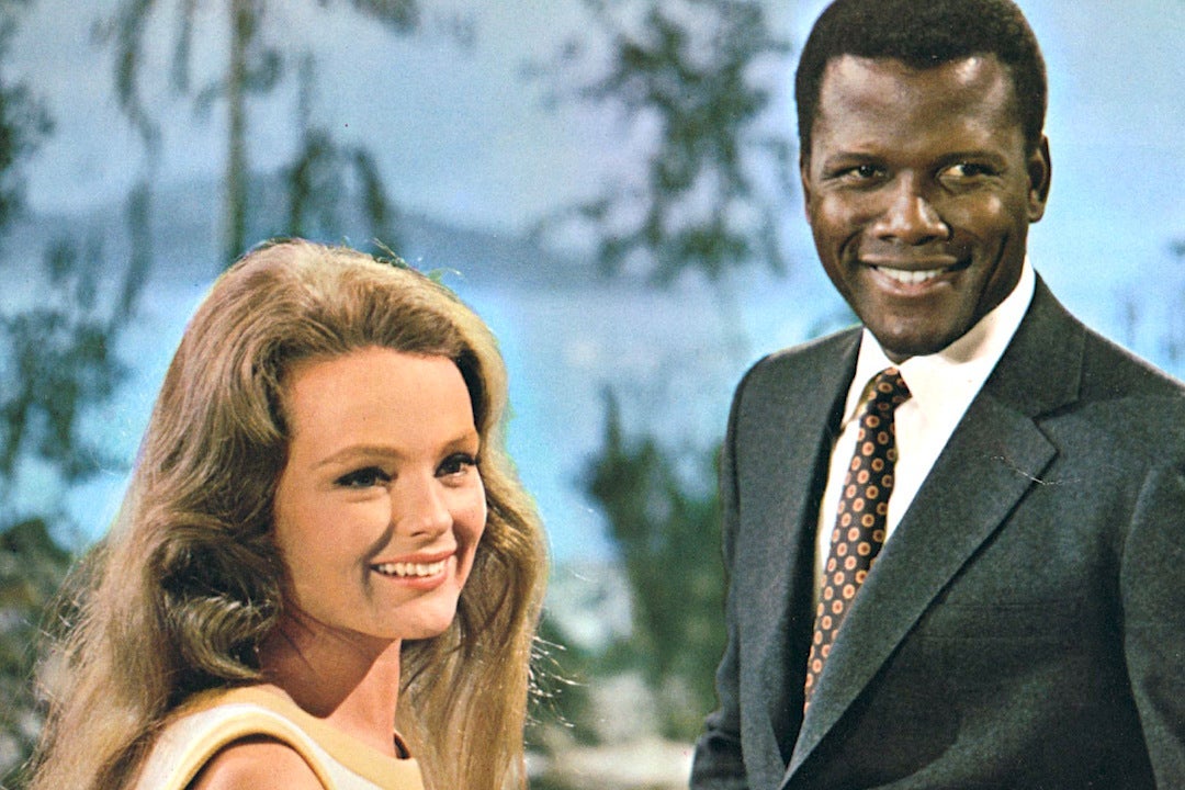 A white woman with brown hair stands next to a black man with a suit and tie on.